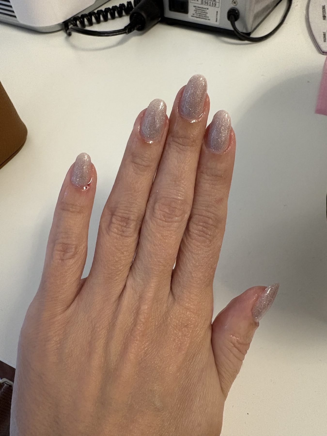 Een hand met parelgrijze, glanzende nagels op een wit bureau